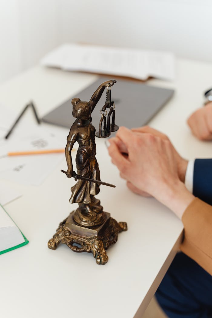 Home Bronze Lady Justice statue on a white office desk with hands in the background. Symbol of law and fairness.